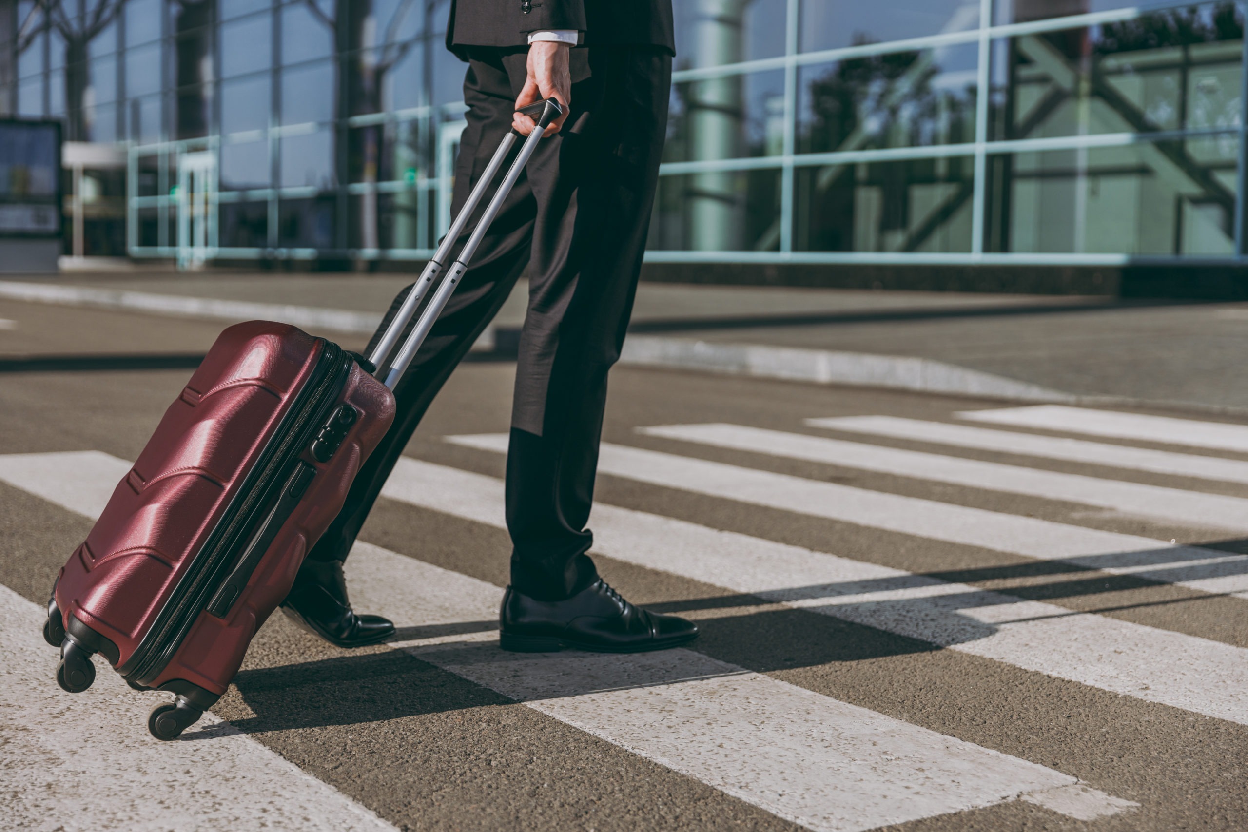 Cropped close up traveler businessman man in black classic dinner suit walk go outside at international airport terminal with bag suitcase valise cross road Air flight business trip lifestyle concept
