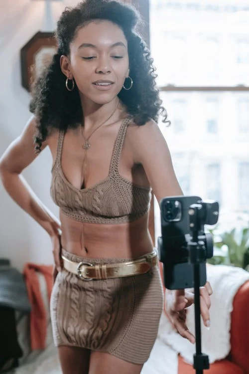a woman in a sexy brown crocheted top and mini-skirt taking video of herself