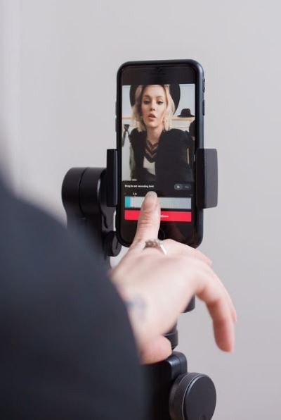 a woman making a TikTok video of herself using her phone propped up by a stand