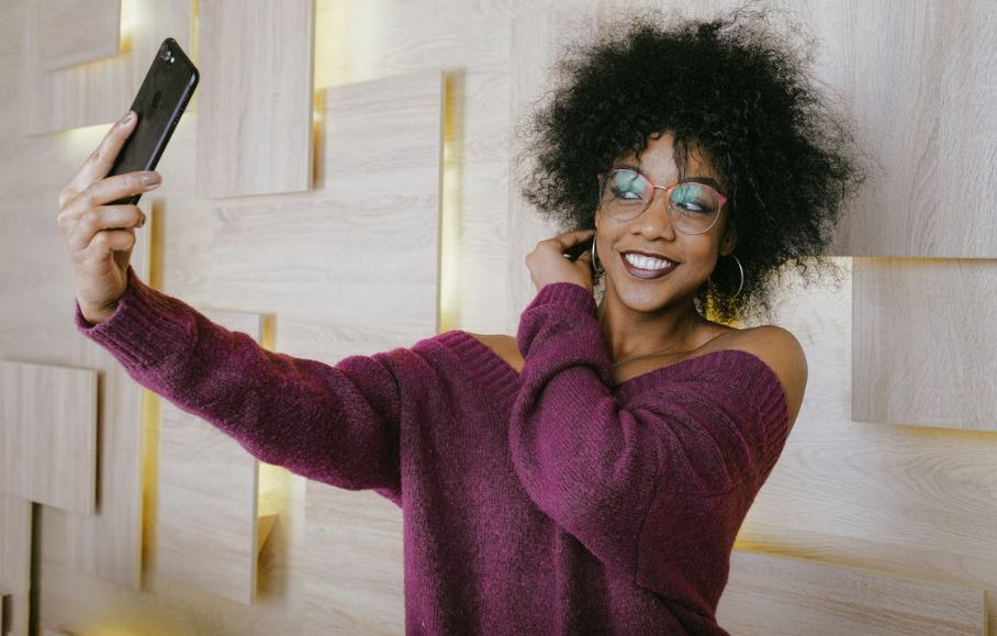 a woman wearing a sweater and eyeglasses taking a selfie