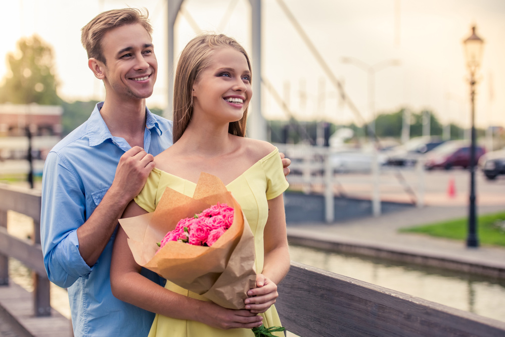 Beautiful young couple on a date is looking away and smiling. Girl is holding flowers