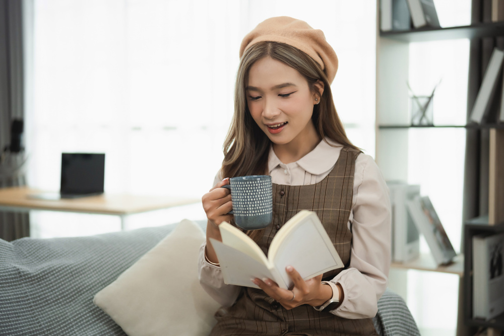 Young woman in cozy setting enjoying a book and a cup of tea while wearing a beret and a plaid outfit, perfect for relaxation and leisure moments