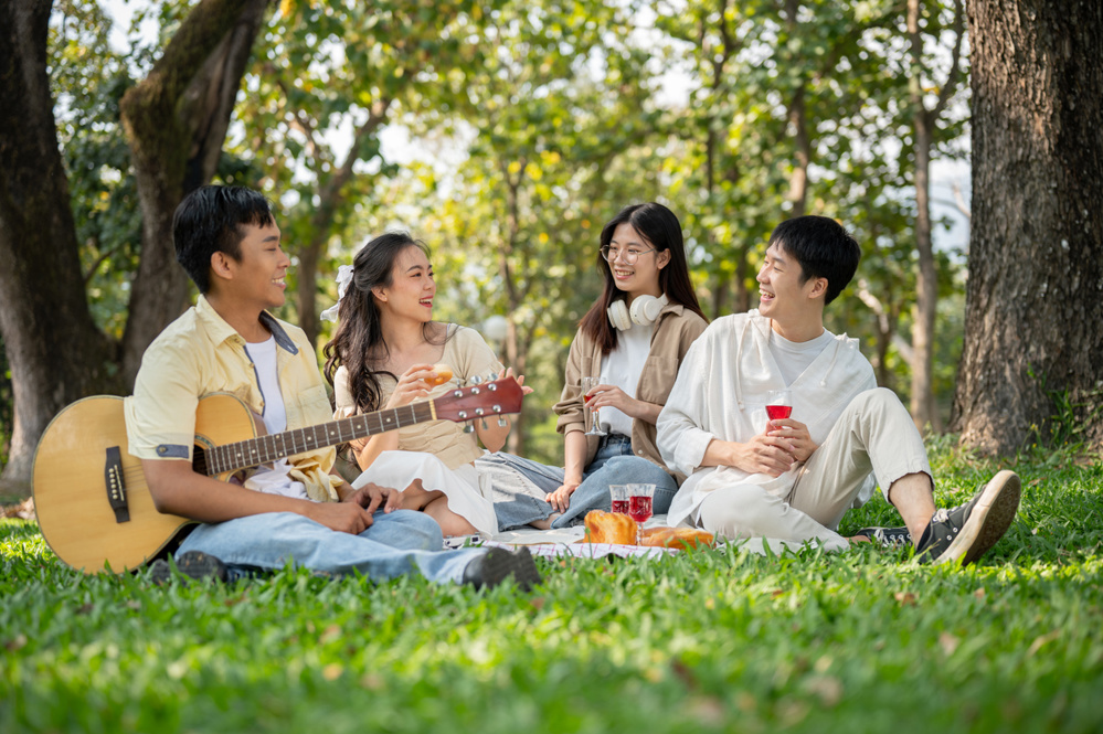 A group of happy young Asian friends is enjoying a picnic in a green park on a summer day together