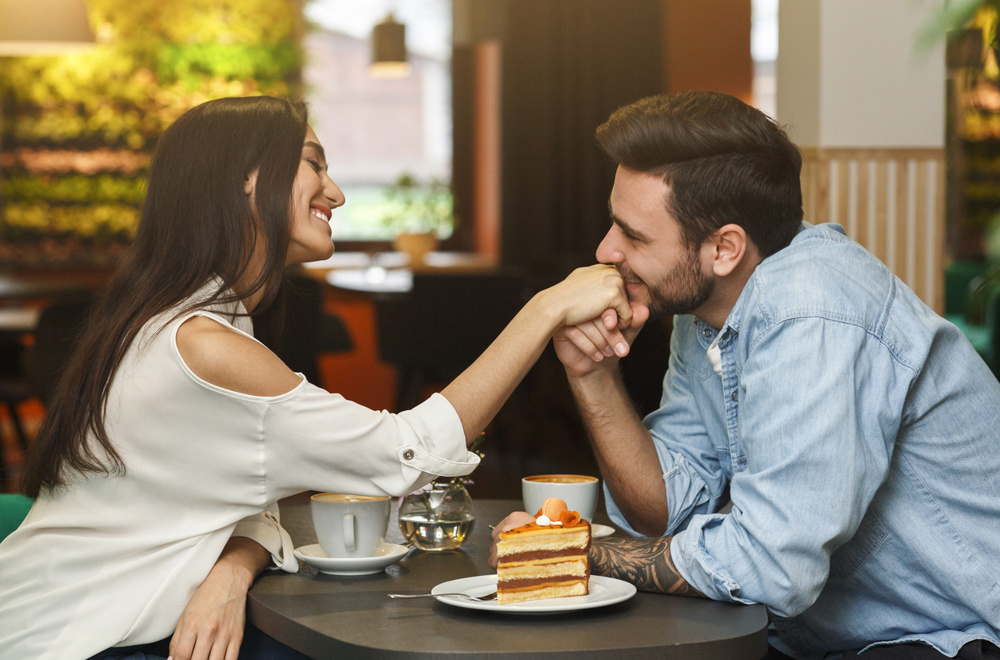 Smiling woman enjoying in a cafe while being kissed in a hand by her boyfriend