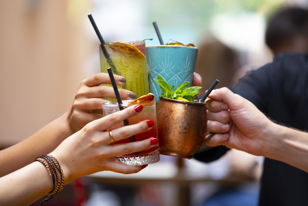 Four hands proposing a toast with yellow and red fruit cocktails
