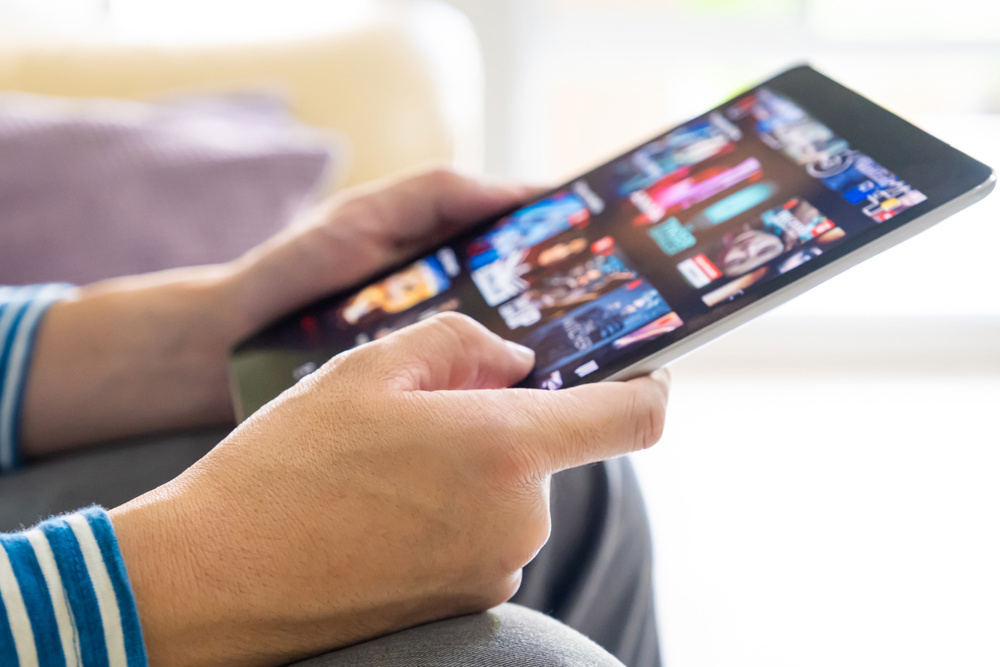 Selective focus at men hand and digital tablet. Young Adult Asian man holding tablet device while choose online movie streaming application with mobile wireless network at home. Entertainment concept