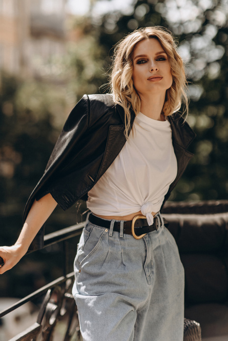 Stylish fashionable blonde woman with smoky eye makeup, in jeans, white t-shirt and black leather jacket on the balcony in the city. Spring autumn fashion concept. Soft selective focus