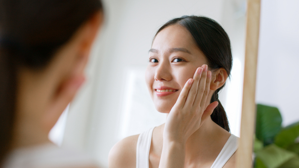 Young Asian beautiful woman touching healthy facial skin look at mirror, Asian beauty skin concept