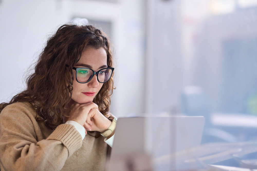 Young woman worker wearing glasses watching online webinar at work