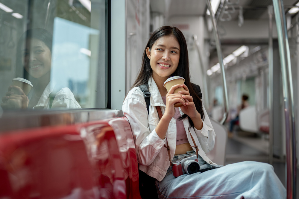 A happy young Asian female tourist is sipping coffee while sitting on a seat in a sky train