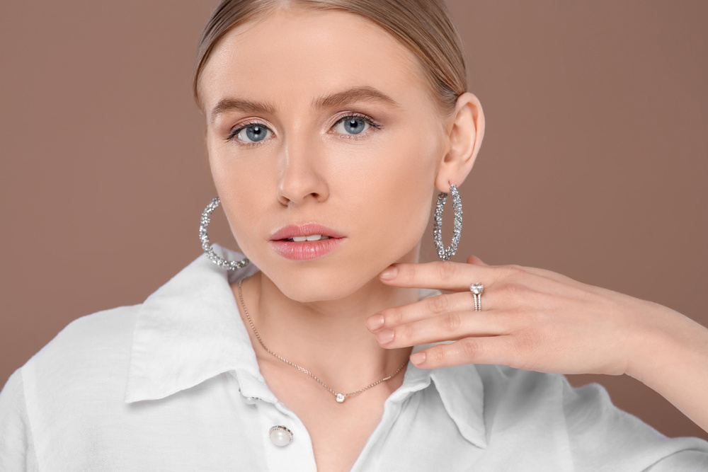 )Beautiful young woman with elegant jewelry on light brown background