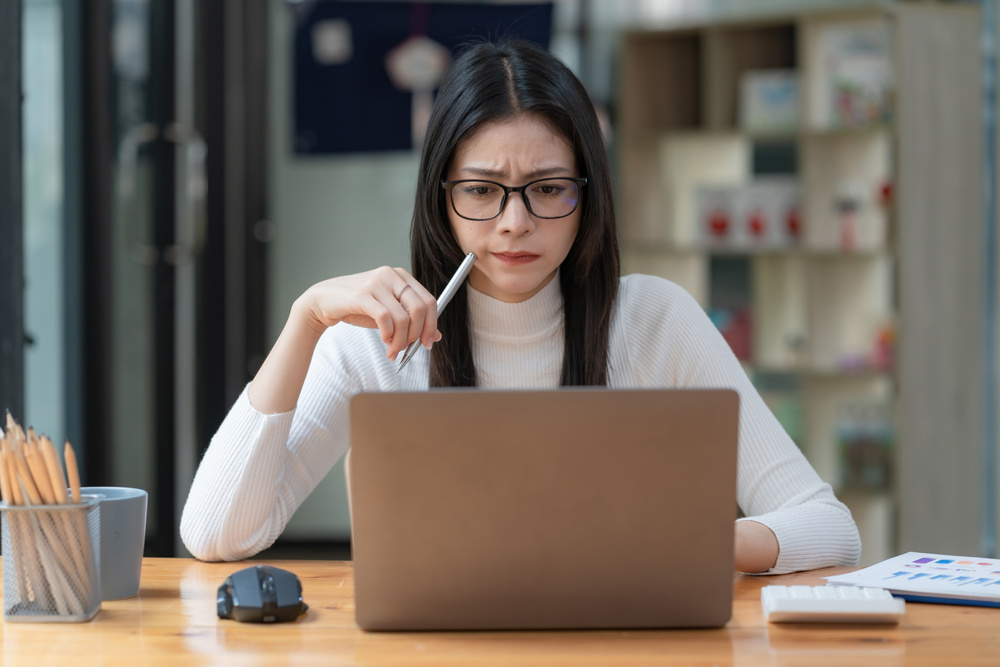Concerned female worker looking at laptop screen suspiciously, thinking about problem-solving, reading ambiguous emails or negative news