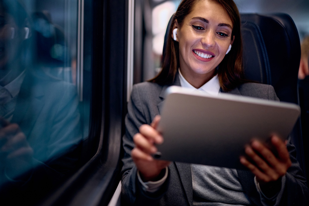 Happy businesswoman using earbuds and touchpad while commuting by train