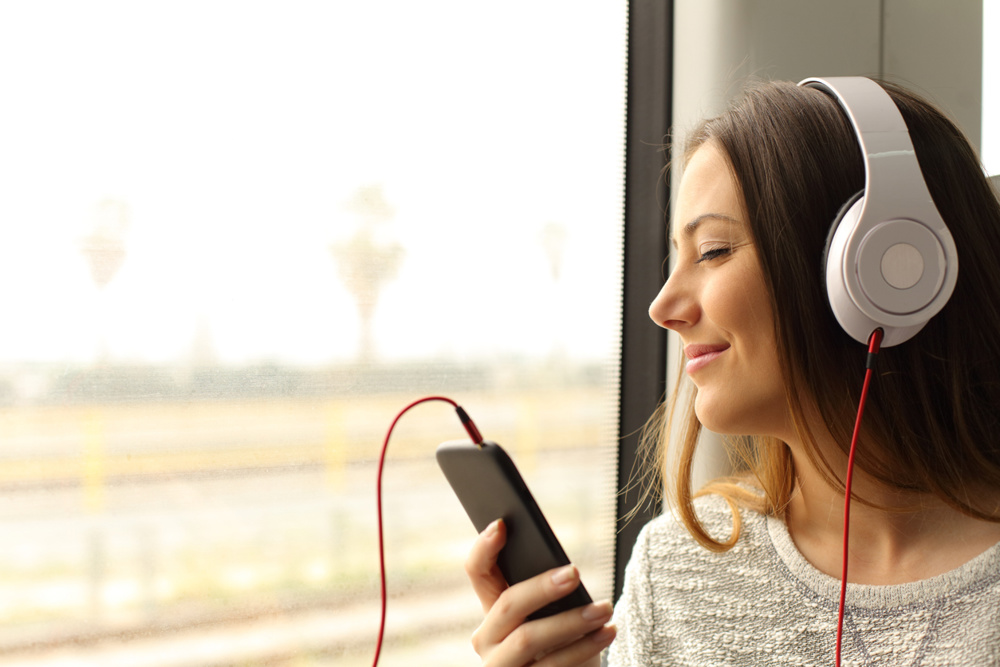 Happy commuter traveling into a train listening to music with a smart phone and headphones