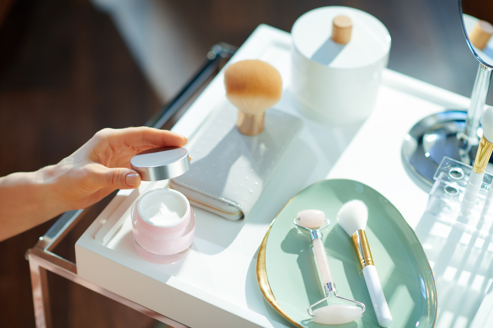 Closeup on housewife opening cosmetic jar on table with toiletries in the living room in sunny winter day