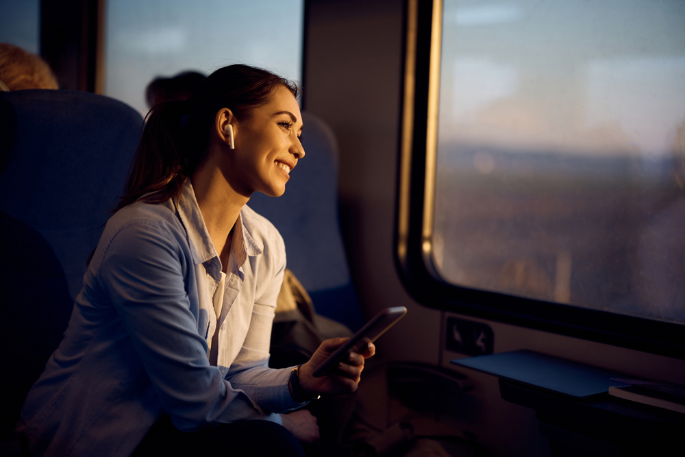 Young happy woman looking through window while traveling by train at sunset