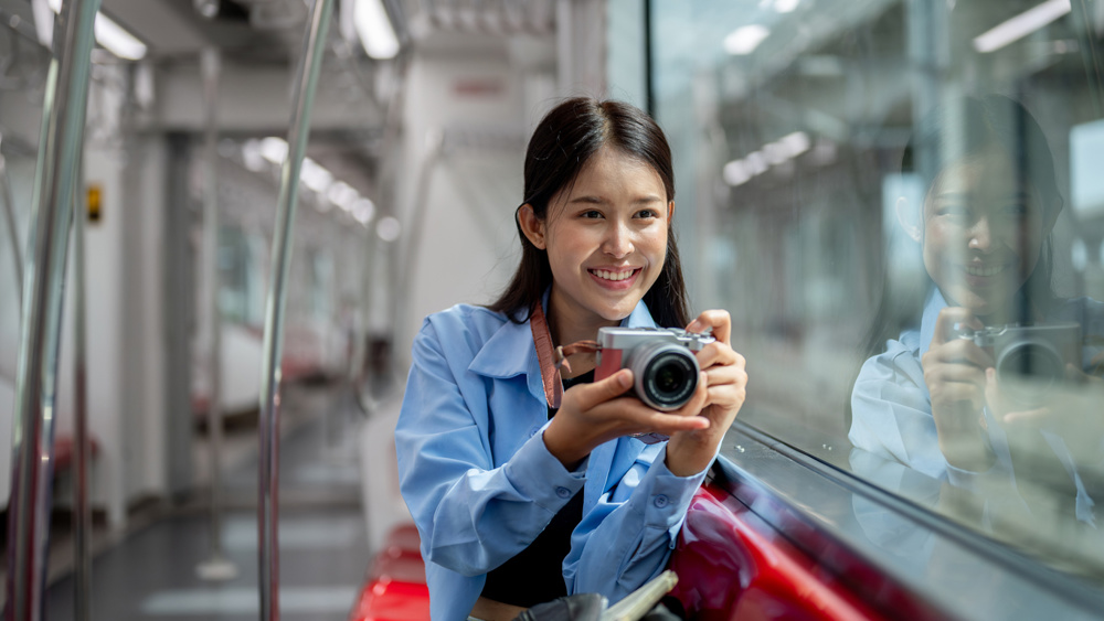 A happy Asian female tourist is taking a picture with her camera while taking the sky train