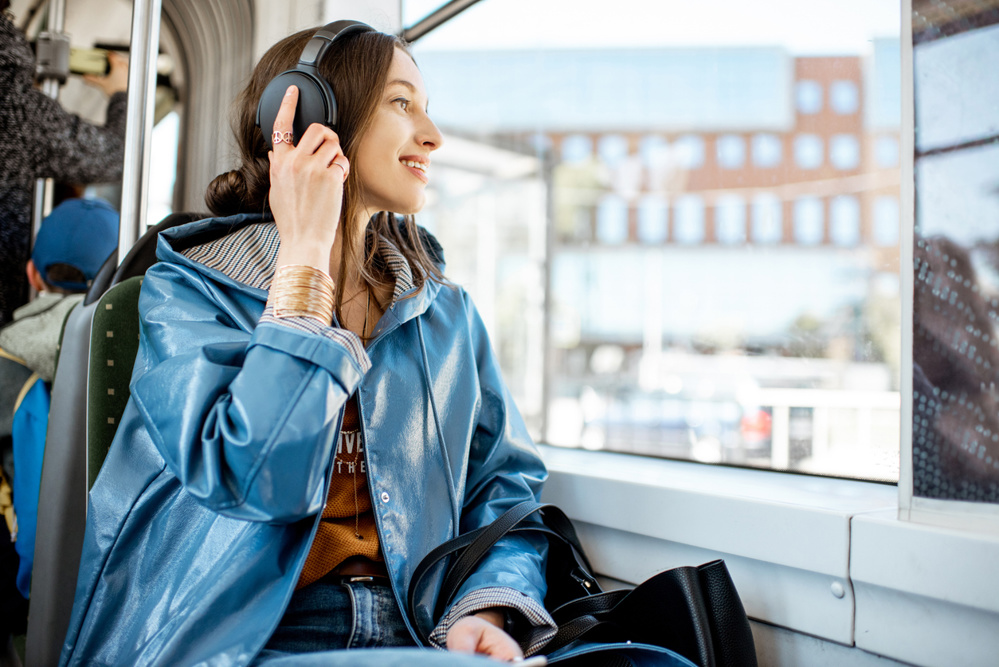 Young woman passenger enjoying trip at the public transport, sitting with headphones near the window in the modern tram