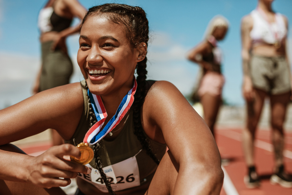 Female runner with a winners medal sitting on track. Running race winner sitting on track with athletes in background