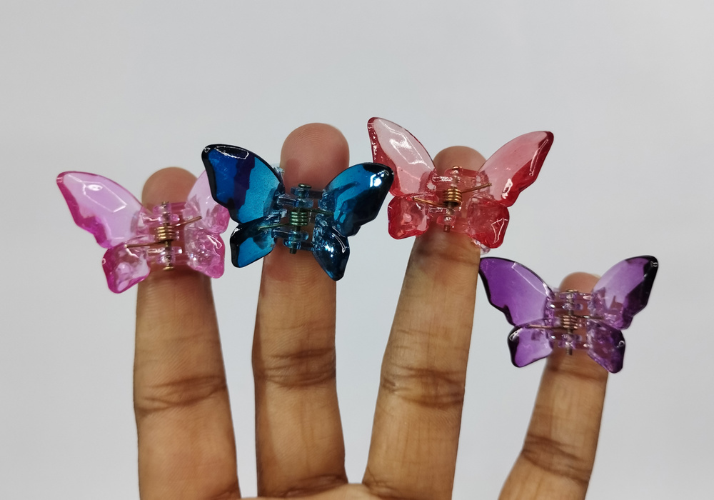 Four small butterfly hair clips are worn on a person's fingers