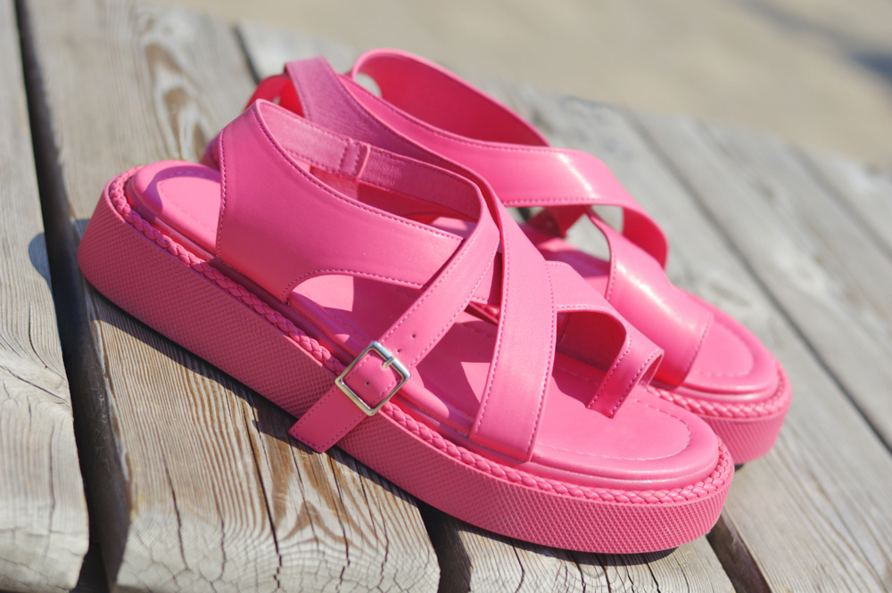 Stylish leather bright pink women's sandals with straps on a wooden bench. Summer women's shoes