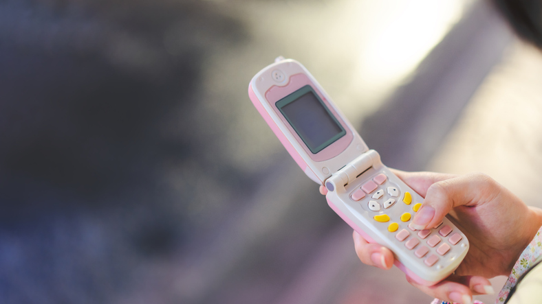Teenager hand using pink flip phone for Y2K nostalgia trend fashion. 2000s vibe with digital gadget concept