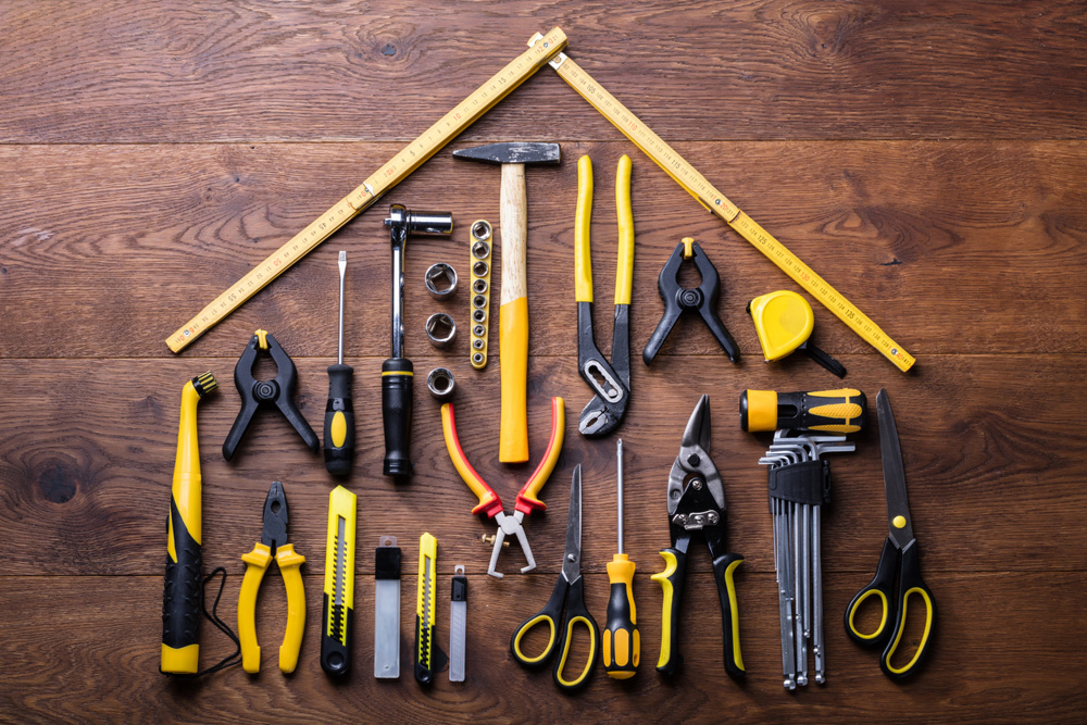 Elevated View Of Many Tools With Roof Made With Yellow Measuring Tape On Wooden Table