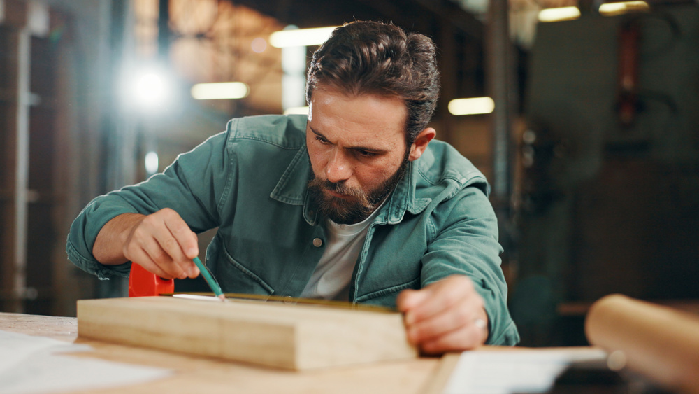 Pencil, carpenter and mark wood to measure for construction, furniture or project. Woodworker, person and plank with tape or tools in creative carpentry workshop for manufacturing, art and craft