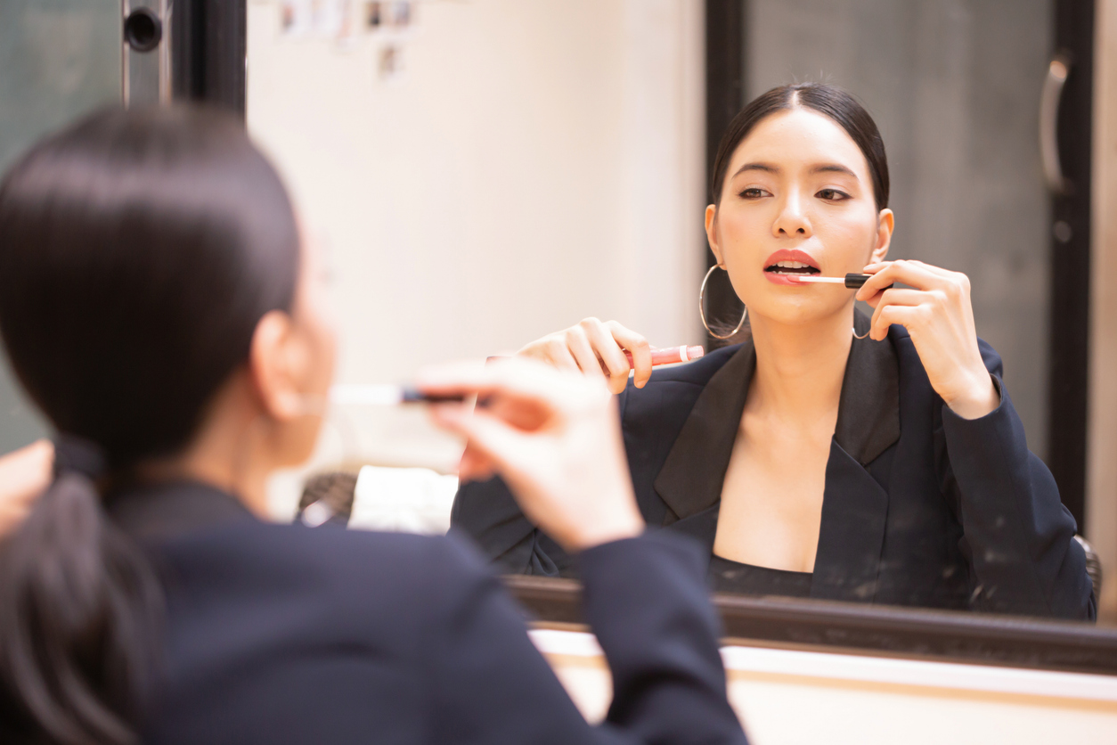 Asian beautiful and elegant girl wearing luxurious black suit putting on lip-gloss cosmetics on lips