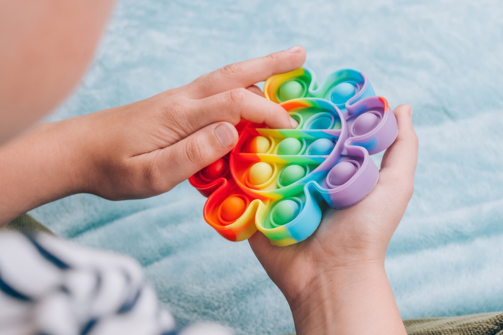Boy playing with rainbow pop it fidget toy. Push bubble fidget sensory toy - washable and reusable silicon stress relief toy. Antistress toy for child with special needs, mental health concept