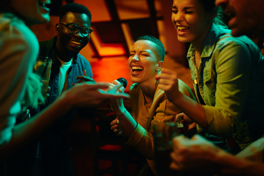 African American woman holding microphone and singing while partying with her friends at nightclub