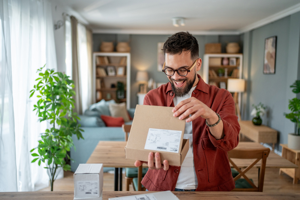 Excited man unboxing a cardboard box filled with his online shopping order, reveling in the joy of home delivery and the convenience of modern retail experiences
