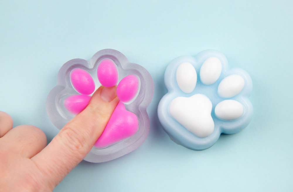Person finger squeezing cute cat paw shape squishy jelly slime toy, studio shot, copy space. Modern popular sensory toy concept