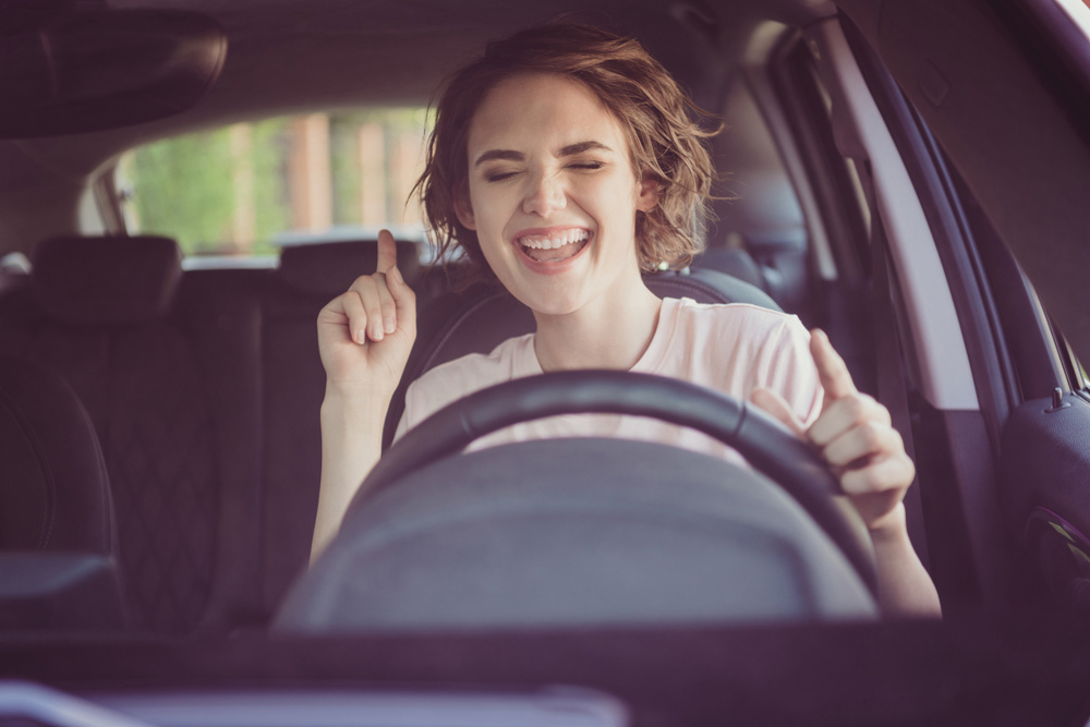 Photo of positive cheerful girl ride drive car town route wait traffic jam listen, music sound try dance feel excited